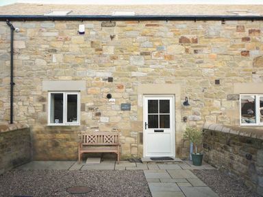 Exterior view of stone building with white door and windows wooden bench and potted plant at The Pepper Pot in Warkworth