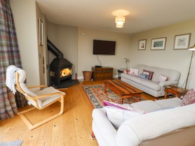 A living room with a wood burning stove wooden floors sofas a wooden coffee table and a wall mounted television at The Mustard Pot in Acklington