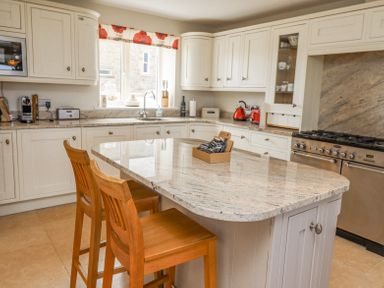 A kitchen with a central island with two wooden chairs and white cabinets at The Mustard Pot in Acklington