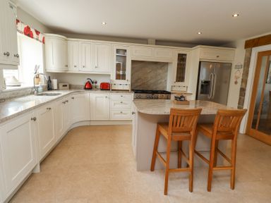A kitchen with white cabinets a marble island countertop two wooden chairs and stainless steel appliances at The Mustard Pot in Acklington