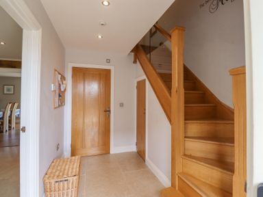 A hallway with wooden staircase a closed wooden door a wicker basket and a bulletin board at The Mustard Pot in Acklington