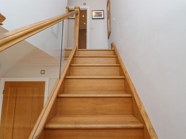 A wooden staircase with glass and wood railing leading to a hallway at The Mustard Pot in Acklington