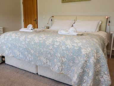 A bedroom with a double bed covered by a floral quilt with towels on top at The Mustard Pot in Acklington
