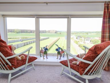 A seating area with two chairs and teddy bears facing a large window with a view of a fenced garden at The Mustard Pot in Acklington