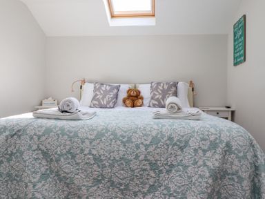 A bedroom with a patterned bedspread rolled towels a teddy bear floral pillows skylight window and bedside tables at The Mustard Pot in Acklington