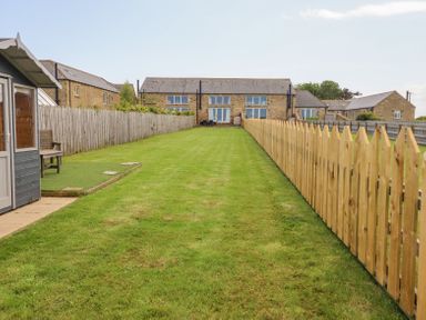 A long grassy garden area with wooden fences on both sides and stone houses in the background at The Mustard Pot in Acklington
