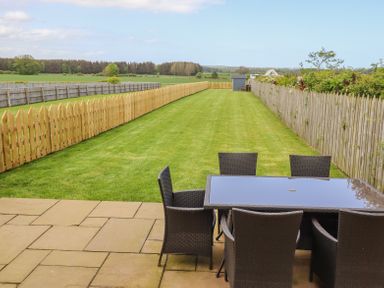A patio with a table and chairs overlooking a long fenced grassy backyard at The Mustard Pot in Acklington