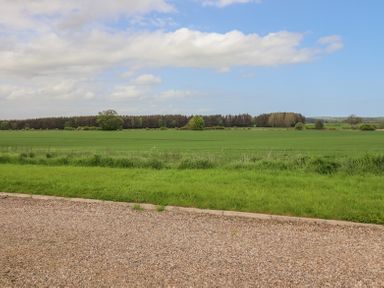 A gravel path leading to a grassy field with trees in the distance under a partly cloudy sky at The Mustard Pot in Acklington