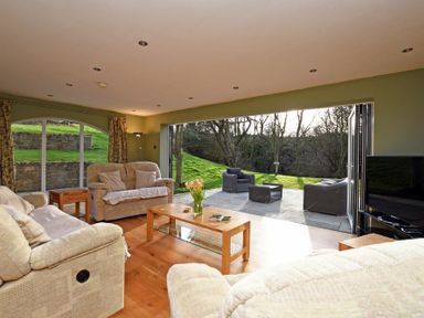 A living room with sofas and a coffee table opening to a patio with outdoor chairs at Quarry Haven in Bamburgh