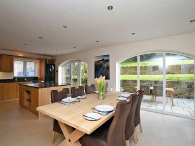 A dining area with a wooden table and chairs next to a kitchen with wooden cabinets and black countertops at Quarry Haven in Bamburgh