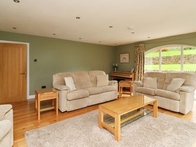 A living room with two beige sofas a wooden coffee table side table and a large window at Quarry Haven in Bamburgh
