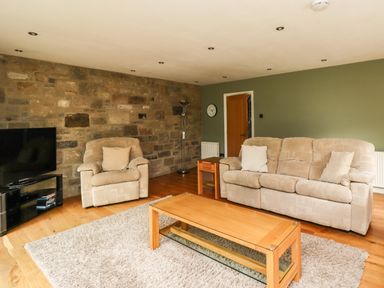 A living room with beige sofas a wooden coffee table and a stone feature wall at Quarry Haven in Bamburgh