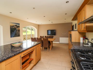 A kitchen and dining area with wooden cabinets a granite countertop a dining table with chairs and a wall-mounted television at Quarry Haven in Bamburgh