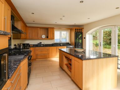 A kitchen with wooden cabinets a black countertop an island and glass doors to the outside at Quarry Haven in Bamburgh