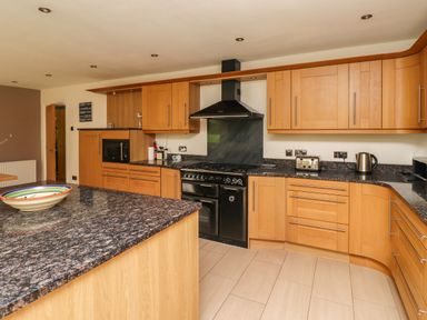 A kitchen with wooden cabinets black countertops a black stove microwave toaster and kettle at Quarry Haven in Bamburgh