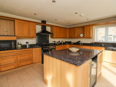 A kitchen with wooden cabinets a black countertop an island with a bowl a stove a microwave and a window at Quarry Haven in Bamburgh