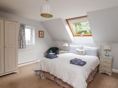 A bedroom with a bed lamps two bedside tables a chair a wardrobe and windows at Quarry Haven in Bamburgh