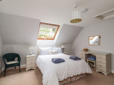 A bedroom with a double bed flanked by nightstands lamps a wicker chair and a dressing table with mirror at Quarry Haven in Bamburgh