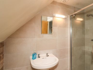 A bathroom with a sink a liquid soap bottle a mirror and a glass shower enclosure at Quarry Haven in Bamburgh