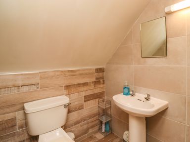 A small bathroom with a toilet and pedestal sink under a sloped ceiling at Quarry Haven in Bamburgh