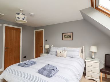 A bedroom with a double bed two folded towels bedside tables with lamps a chair and two wooden doors at Quarry Haven in Bamburgh