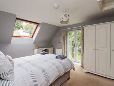 A bedroom with a bed with striped bedding a white wardrobe a desk and double doors leading outside at Quarry Haven in Bamburgh