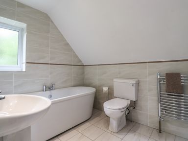 A bathroom with a bathtub, toilet, sink, window, and towel rack with a brown towel at Quarry Haven in Bamburgh