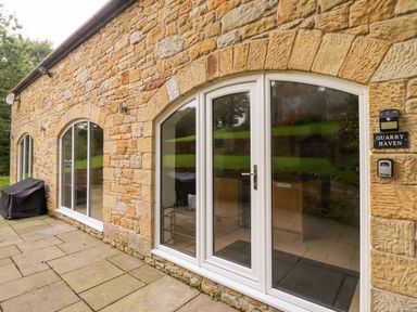 Exterior stone wall with arched glass doors and windows beside a paved patio at Quarry Haven Bamburgh