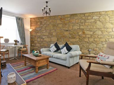 A living room with a stone wall a sofa armchair coffee table and small dining table at Sea Air in Amble