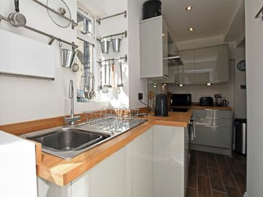 A kitchen with a double sink wooden countertops utensils hanging on the wall and modern appliances at Sea Air in Amble