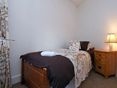 A bedroom with a single wooden bed with floral bedding and a wooden nightstand with a lamp at Sea Air in Amble
