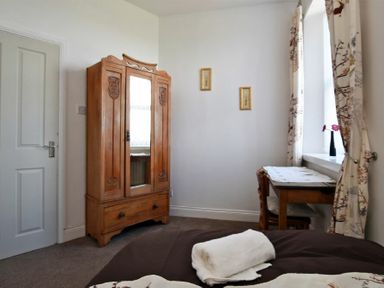 A bedroom with a wooden wardrobe a wooden desk and chair near a window with floral curtains at Sea Air in Amble
