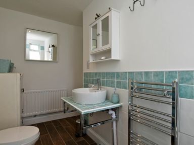 A bathroom with a round basin on a tiled countertop a wall cabinet a mirror radiator and a toilet at Sea Air in Amble