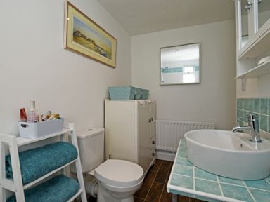 A bathroom with a toilet a white shelving unit with blue towels a white cabinet blue baskets a sink with a tiled countertop and a mirror on the wall at Sea Air in Amble