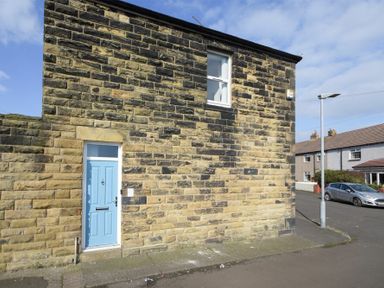 Stone building with a light blue door and one window on a street corner with a street lamp and parked car at Sea Air in Amble
