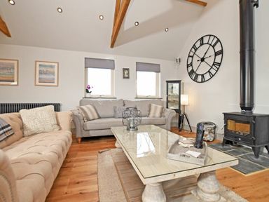 A living room with two sofas a coffee table a wood burning stove and a large wall clock at The Hemmel (Beadnell) in Beadnell