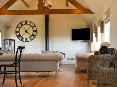 A living room with two beige sofas a black chair a wicker chair a wall clock a wall mounted television and exposed wooden beams at The Hemmel Beadnell