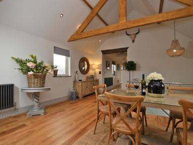 A dining area with a glass table and wooden chairs a wooden sideboard a round mirror flowers in vases and a mounted skull on the wall at The Hemmel Beadnell