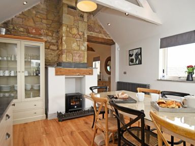 A dining area with a table set for breakfast and a stone fireplace in the corner at The Hemmel (Beadnell) in Beadnell