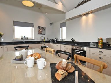A kitchen with a wooden table set with bread and mugs at The Hemmel (Beadnell) in Beadnell