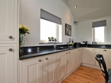 A kitchen with beige cabinets black countertops a sink two windows and wooden floor at The Hemmel Beadnell