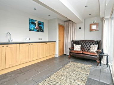 A room with wooden cabinets a leather sofa two cushions a small table and a rug at The Hemmel Beadnell