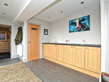A laundry room with wooden cabinets a sink a coat rack and a cow painting at The Hemmel Beadnell