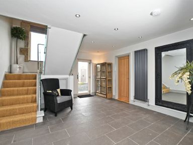An entrance hall with stairs a black armchair a wooden cabinet a large mirror and a wooden door at The Hemmel Beadnell