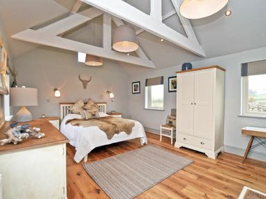 A bedroom with a double bed a wardrobe two windows and wooden floor at The Hemmel Beadnell