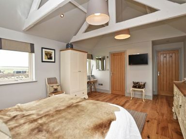 A bedroom with wooden floor a bed with animal print blanket a wardrobe chairs two wooden doors and a wall mounted tv at The Hemmel Beadnell