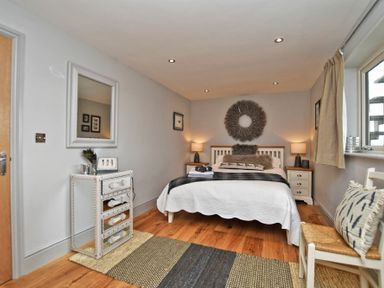 A bedroom with a bed bedside tables a chair and a mirrored chest at The Hemmel (Beadnell) in Beadnell