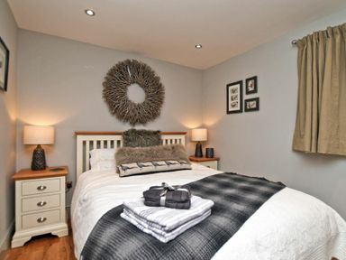A bedroom with a bed between two bedside tables with lamps and a window with curtains at The Hemmel Beadnell