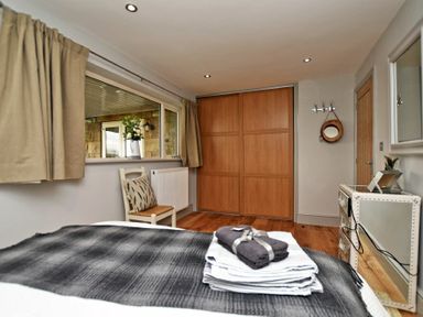 A bedroom with a bed covered with folded towels and a blanket a wooden chair beside a window with curtains and a built in wardrobe at The Hemmel (Beadnell) in Beadnell