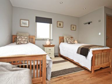 A bedroom with two wooden single beds a striped rug and framed pictures on the wall at The Hemmel in Beadnell